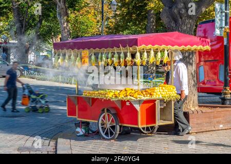 A vendor sells fresh cooked corn on the cob in the Sultanahmet Square district of Istanbul Turkey, as a man with a stroller passes by. Stock Photo