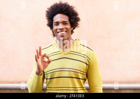 Black man with afro hair putting a funny expression outdoors. Ok gesture with his hand. Black man with afro hair putting a funny expression Stock Photo