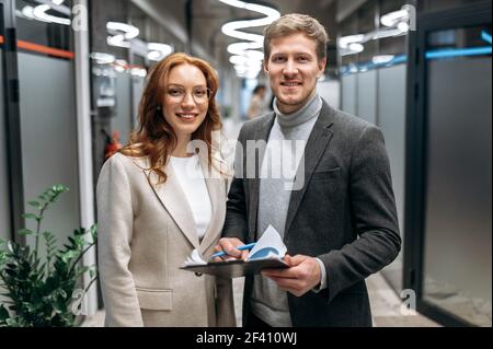 Portrait of happy successful business partners in modern office. Confident colleagues in stylish formal suits are looking directly at the camera and smiling, teamwork concept Stock Photo