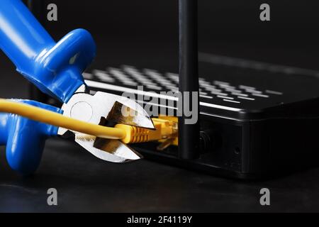 Tearing and cutting with blue wire cutters the network connection of the yellow wire of the Internet connection. Disabling and restricting Internet ac Stock Photo