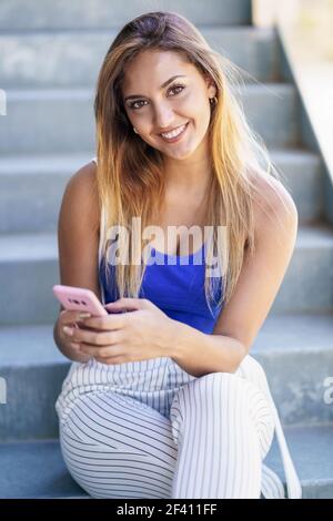 Young woman using a touchscreen smartphone wearing casual clothes. Girl sitting outdoors.. Girl using a touchscreen smartphone wearing casual clothes Stock Photo