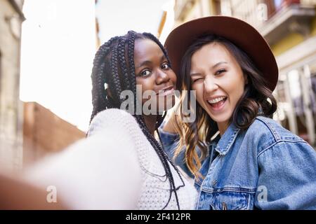 Two multiethnic women making selfie and grimacing with a smartphone.. Two beautiful multiethnic women making selfie and grimacing Stock Photo