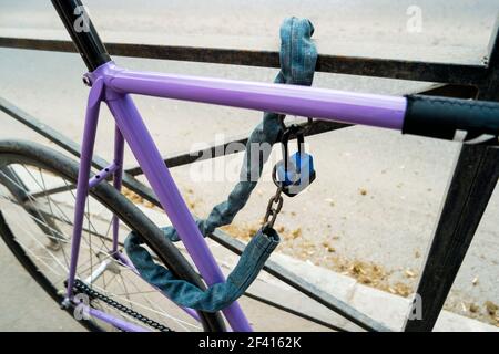 Iron chain and lock on a old bicycle of violet color. Locked bicycle at bicycle outdoor parking space. Iron chain and lock on a old bicycle of violet color Stock Photo