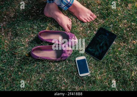 Barefoot girl relaxing on grass with tablet-pc and smartphone. Barefoot girl sitting on grass with tablet-pc and smartphone Stock Photo