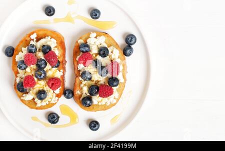 Sandwiches with curd cheese, blueberries, raspberries and honey on white plate. Healthy breakfast. Top view, flat lay Stock Photo