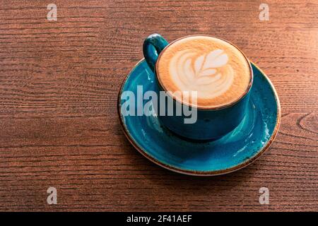 Ideal morning. Cappuccino mig of teal color is standing on wooden tabletop of office desk. Image shot with copy space.. Ideal morning. Cappuccino mig of teal color is standing on wooden tabletop of office desk Stock Photo