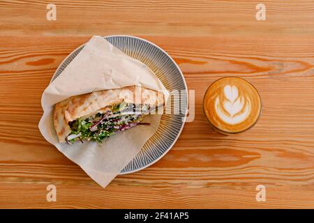 Shawerma sandwich chicken roll in pita on plate with fresh vegetables and flat-white on wooden table top view.. Shaverma sandwich chicken roll in pita with fresh vegetables and flat-white on wooden table top view Stock Photo