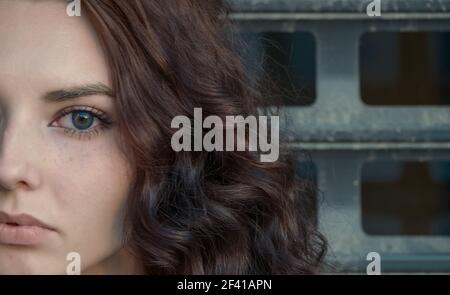 Meditative girl half face in front of metal grid looking at camera, copyspace. Broody girl half face in front of metal grid looking at camera Stock Photo