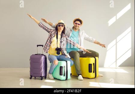 Portrait of young cheerful couple travelers flying like plane sitting on luggage Stock Photo