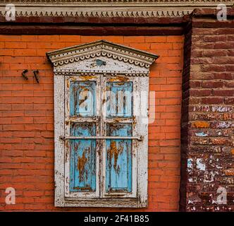 An old wooden carved window with shutters closed on the wall of a brick house Stock Photo