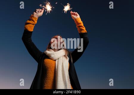 Happy woman with burning sparklers in both hands raised in the dark night sky. Happy woman with burning sparklers in both hands raised in the sky Stock Photo