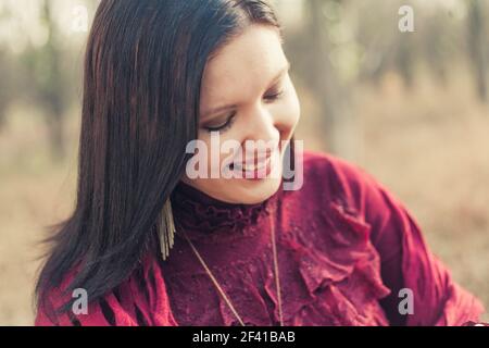 Happy woman in red dress smiling looking down in front of nature background Stock Photo