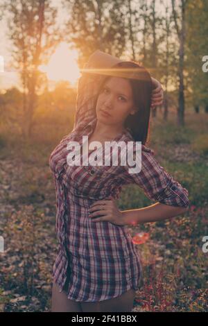 Calm girl posing in woodland park in autumnal time at sunset dressed in checkered shirt. Stock Photo
