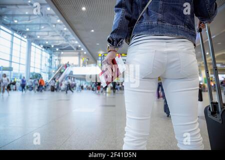 Female Traveller holds a passport and a ticket against the background of the airport hall Stock Photo