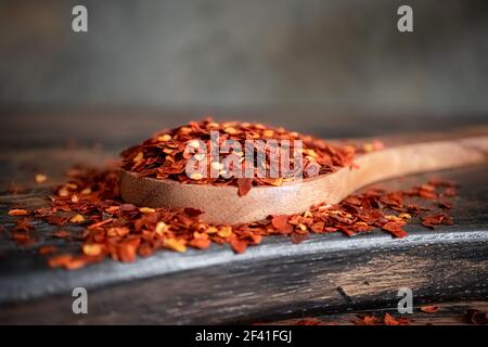 Flakes of red hot chili pepper in wooden spoon closeup on a kitchen table. Stock Photo