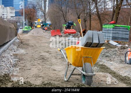 Construction wheelbarrow and curb concrete blocks against the background of a city street in blur. Stock Photo