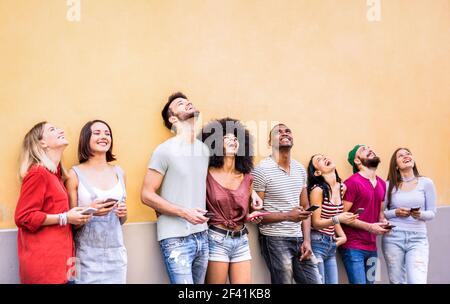 Multiracial friends having fun using smartphone at wall on university college break - Young people addicted by mobile smart phones Stock Photo