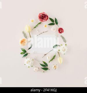 Creative spring Easter  frame made with  colorful  spring flowers and green leafs with  paper card note over pastel beige  background.  Minimal flat l Stock Photo