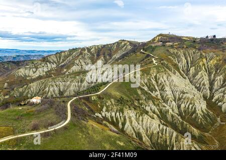 Aerial photograph of the worst soil erosion and olive plants in Abruzzo, showing a lengthy, winding road near a cottage on a peak Stock Photo