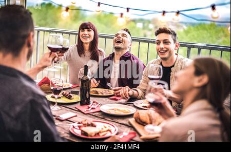 Young friends having fun drinking red wine at balcony penthouse dinner party - Happy people eating bbq food at fancy alternative restaurant together Stock Photo