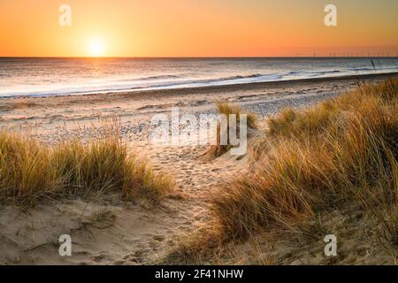 A sandy winding path weaves through the sand dunes and towards the sea on the Norfolk Coast at Winterton on Sea as the early morning sun rises above t Stock Photo