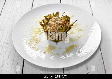 Baked artichoke stuffed with cheese and vegetables in white plate isolated on white painted wooden boards Stock Photo