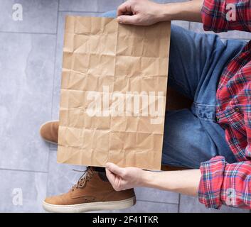 Men's hand holding wrinkled old craft paper blank. Male hand and crumpled paper, top view Stock Photo