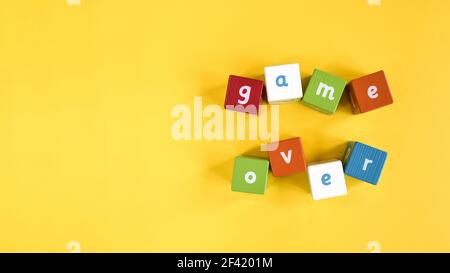 Words Game Over made from colored wooden blocks. Painted cubes with letters on yellow background. They are arranged randomly at different angles. Stock Photo