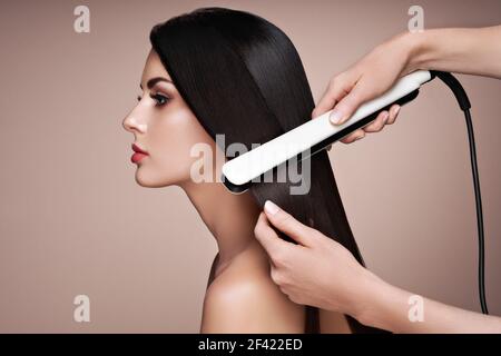 Hairdresser straightening long dark hair with hair irons. Beautiful woman with long straight hair. Smooth hairstyle Stock Photo