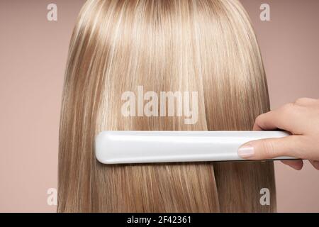 Hairdresser straightening long dark hair with hair irons. Beautiful woman with long straight hair. Smooth hairstyle Stock Photo