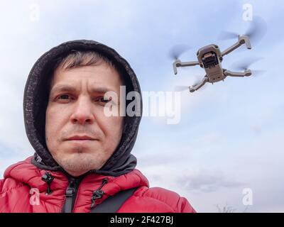 Man controls the flying drone. Grey drone with camera flying in the air outdoors. Little drone flying outside in sky. Stock Photo