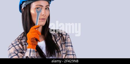 Banner, long format. Caucasian closeup portrait of happy smiling beautiful charming young lady in a helmet looking at camera through wrench tools on Stock Photo