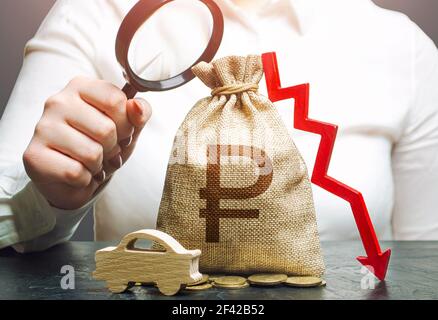 Woman female manager examines a russian ruble money bag with a red down arrow and automobile. Fuel excise taxes. Electric vehicle support subsidies. C Stock Photo