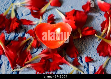 Red carnation petals and a heart shaped candle Stock Photo
