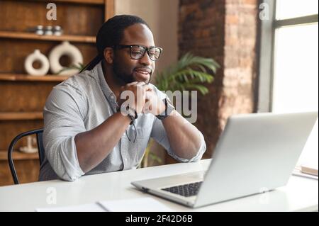 Thoughtful african businessman focused while checking documents in laptop, sitting in his cabinet at home, freelance lawyer, preparing a speech, consulting client online, anylize the statistic Stock Photo