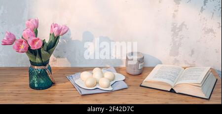 Easter eggs, book and pink tulips on table. Simple holiday image Stock Photo