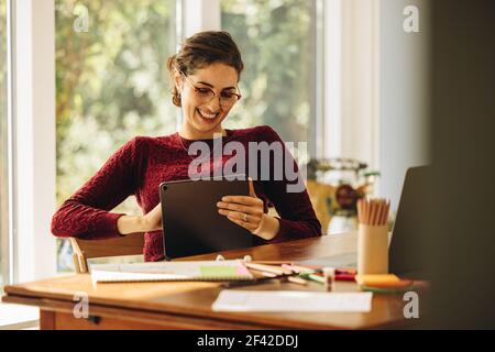 Woman illustrator sitting at home and smiling with a digital tablet. Female designer working at home using tablet pc. Stock Photo
