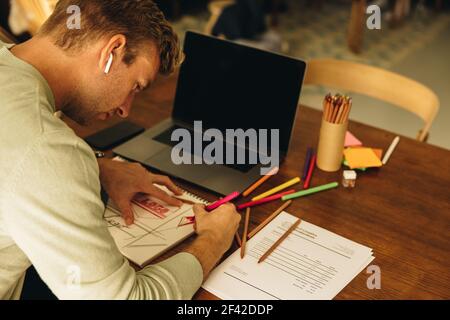Man working at home drawing designs on a paper with a colored pencil. Male designer preparing illustrations. Stock Photo