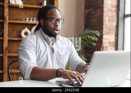Upset business man working with laptop computer in office, feeling stressed and anxious for possible data loss. Adult Hispanic executive under stress at work for technology problems and software pc Stock Photo