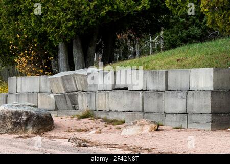 A concrete retaining wall that is falling over. Grass is above the wall, sand below. Several blocks are pushed out and leaning over. Stock Photo