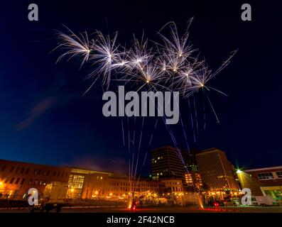 Fireworks. Wide angle shot showing the launch as well as the blooms. Buildings and street lights in the background. Focus is on the fireworks. Stock Photo