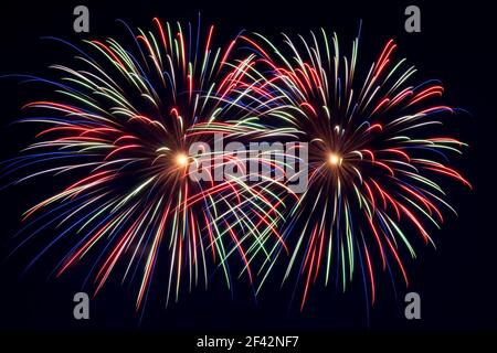 Closeup of fireworks in the sky. Two bright multi color blooms. The sky is very dark blue behind. Stock Photo