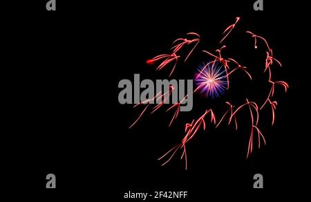 Closeup of fireworks in the sky. Red and blue streamers. Short exposure that results in a small bloom. Room for text on the left. Stock Photo