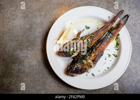 Two fried sea goby fish on white plate with lemon close-up. Mediterranean cuisine, junk food, tasty snacks for beer concept Stock Photo