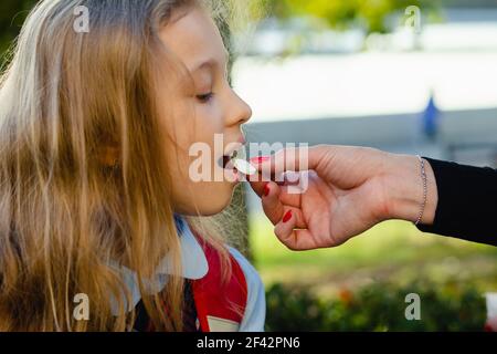 Young mother giving vitamin pill to her little cute daughter, outdoors. Useful for proper development. Hypovitaminosis. Stock Photo