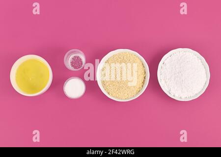 Bowls with ingredients for making homemade French Macaron sweets showing powdered sugar, ground almonds, egg white, salt and sugar on pink background Stock Photo