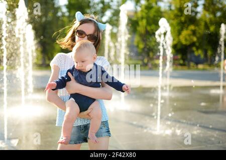 Cute big sister holding her baby brother by city fountain. Adorable teenage girl playing with her baby boy brother. Kids with large age gap. Children Stock Photo