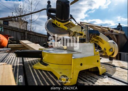 Close up of yellow saw sat on wooden decking being used to construct wooden gazebo roof Stock Photo