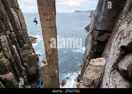 Female rockclimber falls as she tries to climb The Totem Pole, an exposed sea stack which rises out of the ocean in Cape Hauy, Tasman National Park, Tasmania, Australia. Stock Photo