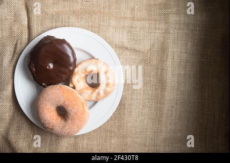 Overhead View of Three Donuts on Round White Plate Against Burlap Stock Photo